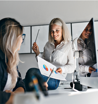 smiling-blonde-female-manager-holding-infographic-pencil-while-sitting-table-indoor-portrait-two-women-working-with-computer-office